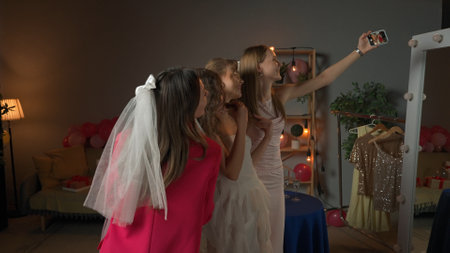Group of young women friends celebrating bachelorette party at home, bridesmaids and bride taking...