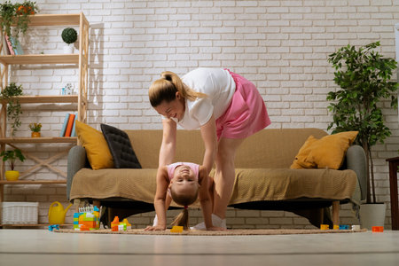 Young mother and daughter on the floor at home spending time together, girl showing gymnastic element bridge, mom helping, full shot.の写真素材