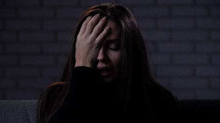 Silhouette of woman with mental health issues, sitting on the sofa, depressed expression, closing face with hands crying, close shot.の写真素材