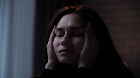Silhouette of woman with mental health issues, sitting on the sofa, depressed expression, tired face, holding head with hands, close shot.の写真素材