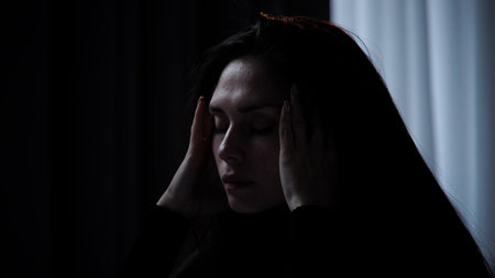Silhouette of woman with mental health issues, sitting on the sofa, depressed face expression, having headache, holding hands on head temple, tired face close shot.の写真素材