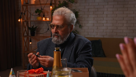 Family sit at table at home, grandchildren and parents celebrating birthday of grandfather, grandpa got vintage pocket watch as present.の写真素材