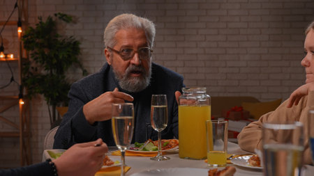 Family sit at table at home, grandchildren and parents celebrating birthday of grandfather, family members enjoying meal, close up of grandpa talking.の写真素材