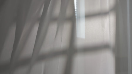 Transparent white silk soft fabrics floating with light shining through, shades shadows of window silhouette reflected on the textile.の写真素材