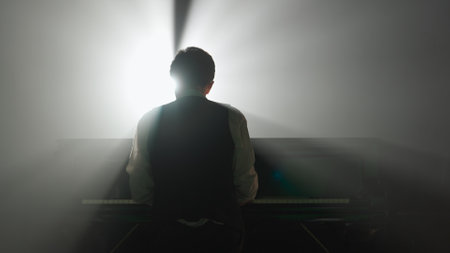 Pianist playing on the black grand piano on dark concert stage against spotlight, back shot isolated on black studio background. Artist performing in concert hall.の写真素材