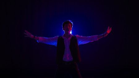 Man musician in stylish hat dancing on dark concert stage against blue spotlight and singing looking at camera, isolated on black studio background.の写真素材