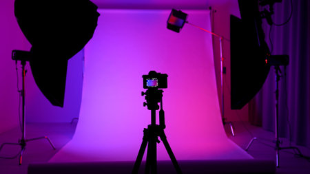 Professional studio for photo and video production filming with modern lighting equipment, cyclorama background colored with pink neon light, camera on tripod.の写真素材