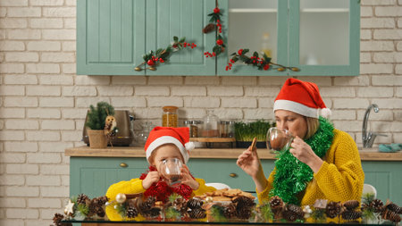 Mother and daughter in the christmas decorated kitchen, mom teaching girl making gingerbread cookies, mom and girl wearing santa hats eating cookies and drinking cocoa.の写真素材