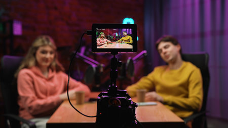 Man host and woman guest recording interview in loft podcast studio using microphones and smartphone...