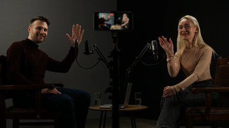 Man host and woman guest recording interview in stylish podcast studio using microphones and...