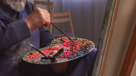 Elder man spending his free time with hobby, visiting art studio class, painting picture with paintbrush on an easel, close up of palette. Daily routine lifestyle concept.の写真素材