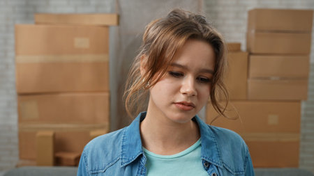 Young couple moving into new apartment, space filled with cardboard boxes, woman stands in the room, looks at boxes with stuff.の写真素材