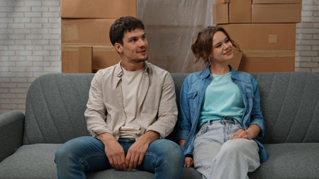 Young couple moving into new apartment, space filled with cardboard boxes, man and woman sit on the sofa in the room of new apartment, happy positive expression.の写真素材