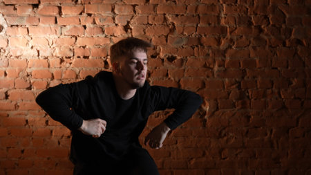 A dancer in black clothes performing against a red brick wall