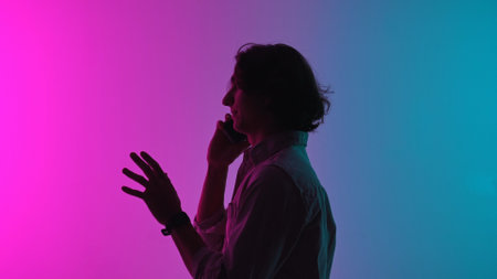 Portrait of man silhouette in casual clothing talking on smartphone, standing isolated on pink blue neon studio background.の写真素材