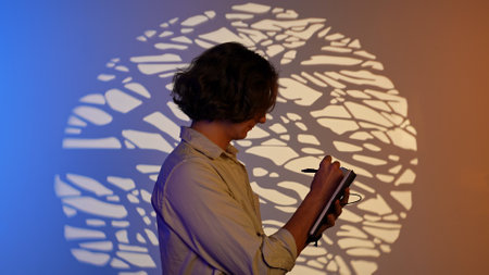 Portrait of man holding writing in notebook, standing in spotlight isolated on blue orange neon with...