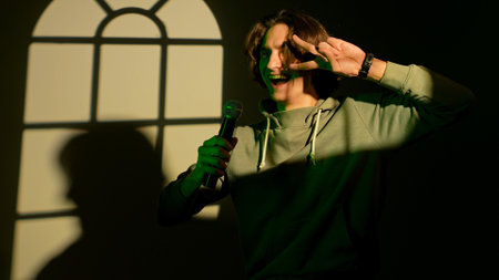 Portrait of man in green neon singing in karaoke microphone, standing in spotlight isolated on dark...