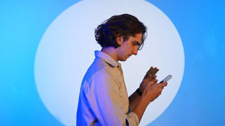 Portrait of man typing card number on smartphone, shopping online, standing in spotlight isolated on...