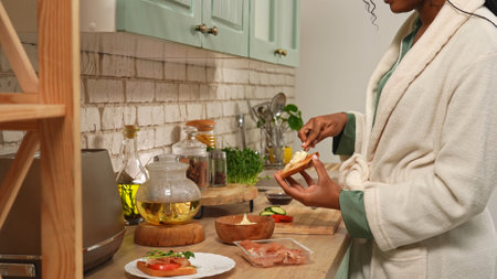 Young african american woman in the morning at the kitchen preparing healthy breakfast, woman prepares toasts, spreading soft cheese on the bread with knife.の写真素材