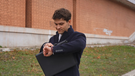 Young businessman in the morning enjoying his daily walk to the office in the city, walking on the street checking time looking at watch, smiling positive expression.の写真素材