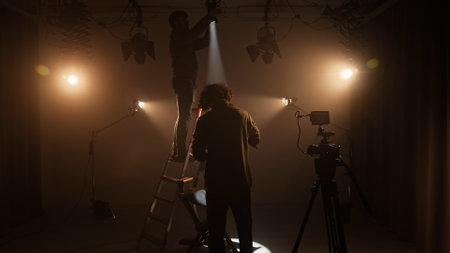 Studio for photo video production filming with lighting equipment and cyclorama, team members fixing lights standing on the ladder.の写真素材