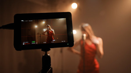 Studio for photo video production filming with lighting equipment, focus on woman singer in red...