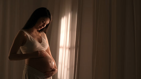 Young happy Asian pregnant woman posing in studio with white curtains in backgroundの写真素材