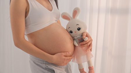 Young happy pregnant woman posing in studio with white curtains in backgroundの写真素材