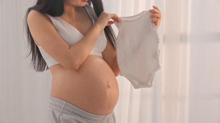 Young happy pregnant woman posing in studio with white curtains in background