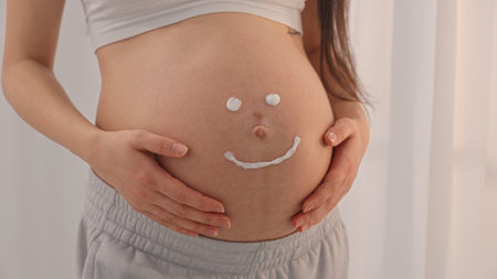Young happy pregnant woman posing in studio with white curtains in backgroundの写真素材