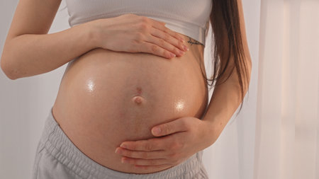 Young happy pregnant woman posing in studio with white curtains in background