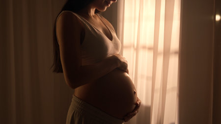 Young happy pregnant woman posing in studio with white curtains in background