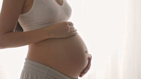 Young happy pregnant woman posing in studio with white curtains in backgroundの写真素材
