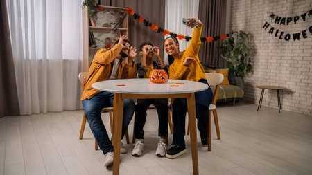 African american family of mom, dad and little son preparing for halloween celebrations, sitting at table taking selfie on smartphone together and having fun.の写真素材