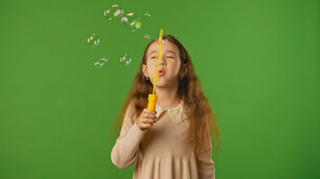 Little girl blowing in soap bubble stick maker, bubbles flying around, positive expression, isolated on chroma key green screen studio background mockup.の写真素材