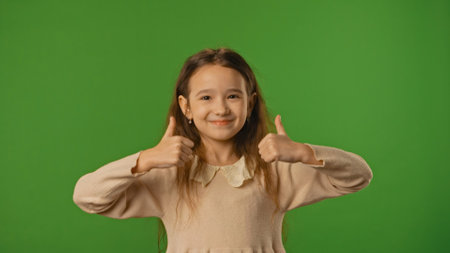 Little girl child looks at camera and shows thumb up hand sign, positive expression, isolated on chroma key green screen studio background mockup.の写真素材