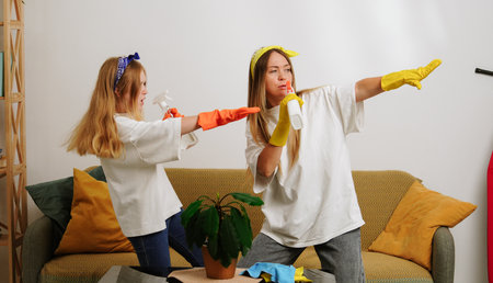 Mother and daughter cleaning the room, holding dust brushes, dancing singing and having fun. Mom teaching little girl how to keep the house clean.の写真素材