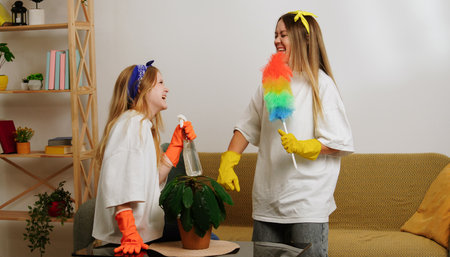 Mother and daughter cleaning the room, wiping dust with brushes, laughing and having fun. Mom...