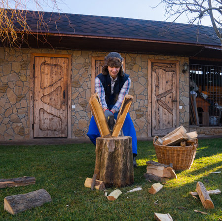 Young couple spending day outside at backyard preparing firewood for winter, shot of man chopping wood with an axe on a wooden stump, positive expression,の写真素材