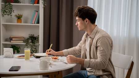 Young man in the morning in the kitchen dinning room enjoying healthy breakfast, sits at table...