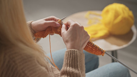 A woman knitting needles from orange yarnの写真素材