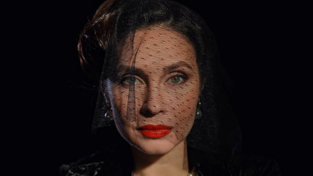 Woman actress in retro outfit with pin-up hairstyle and makeup posing at camera isolated on black...