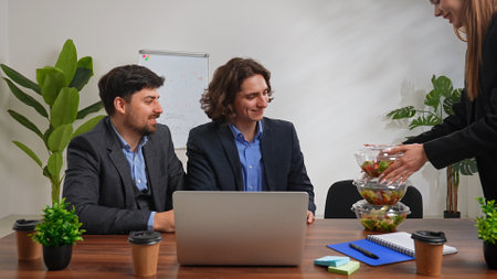 Business team of men and woman working at desk in the office having dinner break with food delivery,...