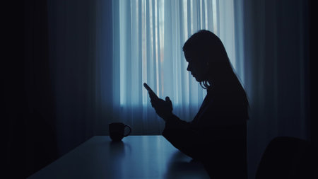Silhouette of a Woman Engaging with Her Smartphone Indoorsの写真素材