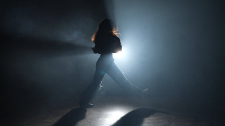 Silhouette of a woman dancing jazz-funk in a studio. Black background filled with smoke, white...