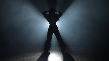 Silhouette of a woman dancing jazz-funk in a studio. Black background filled with smoke, white...