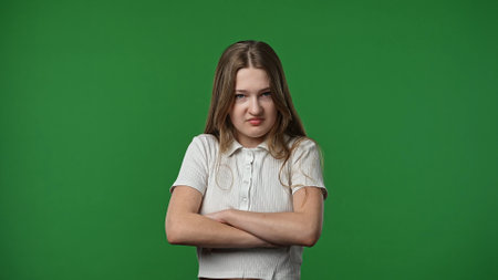 Teenage girl posing at camera with crossed arms and mad upset frustrated face, negative expression,...