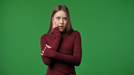 Teenage girl posing at camera looking away with concentrated face and thinking, focused expression, isolated on chroma key green screen studio background mockup.の写真素材