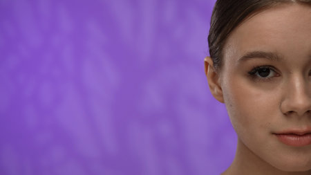 Young woman with makeup posing at camera in studio, smiling visible half of the face, close up...