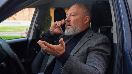 Elderly man behind the wheel of a car talking on a smartphoneの写真素材